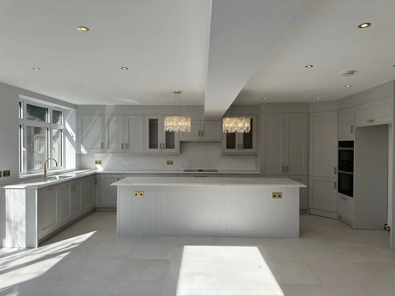 Open-plan shaker kitchen with panelled island, quartz worktops and chandeliers by Alb Homes in Hampstead