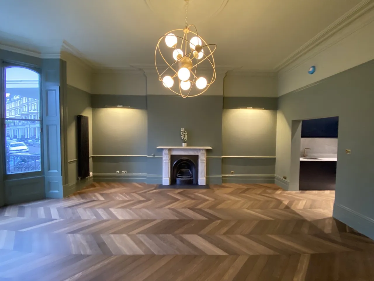 Renovated period reception room with panelled sage walls, marble fireplace and chevron parquet by Alb Homes in Kensington