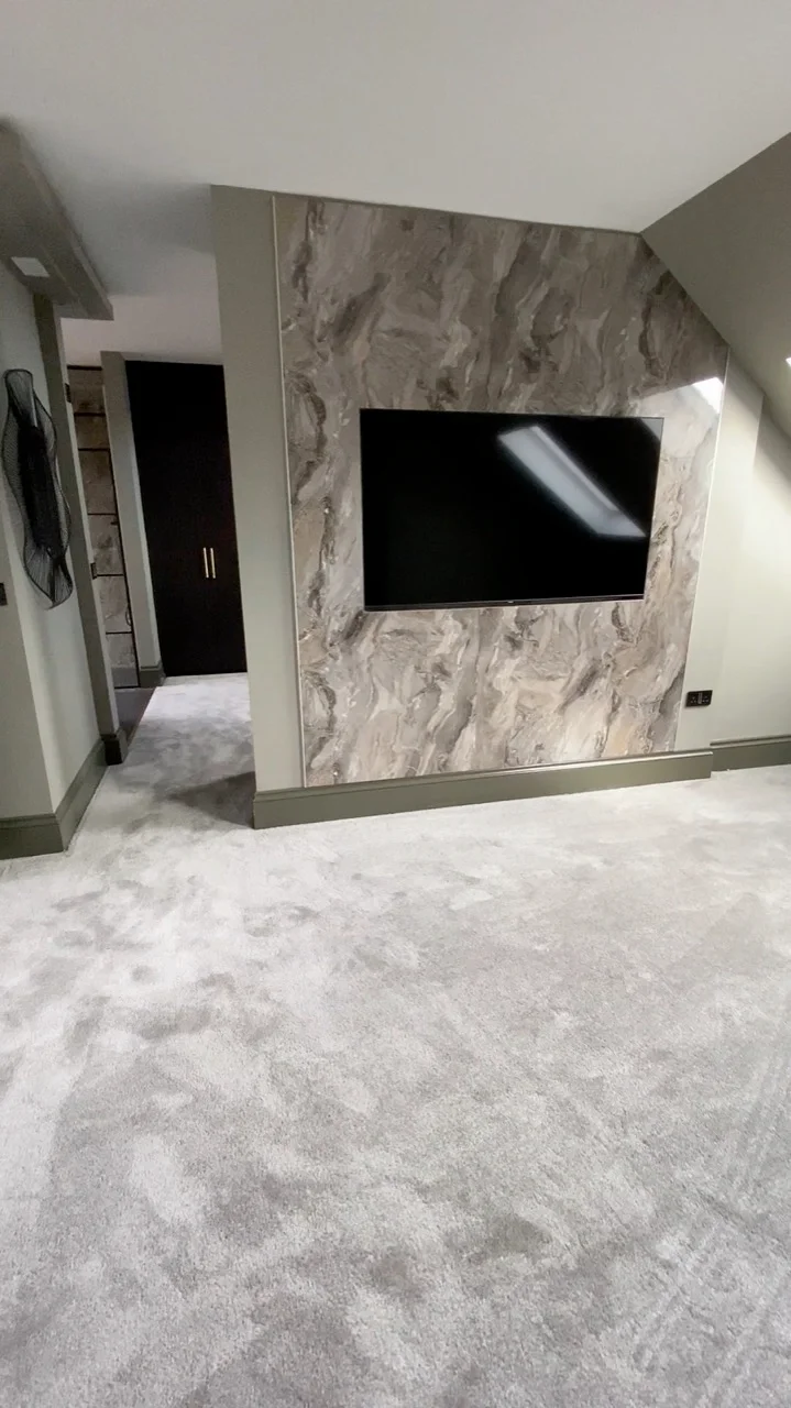 Converted loft bedroom with marble-effect media wall and mounted TV by Alb Homes in Whetstone